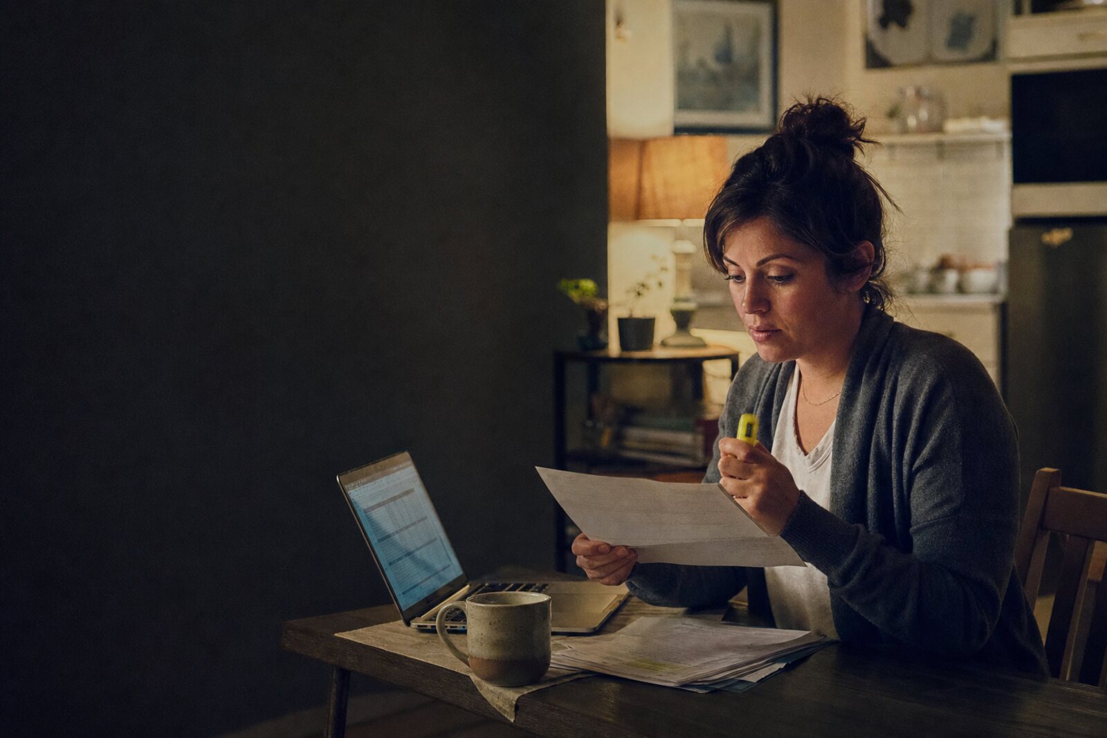 A woman at her kitchen table at night reading her student loan servicer letter with a highlighter in hand